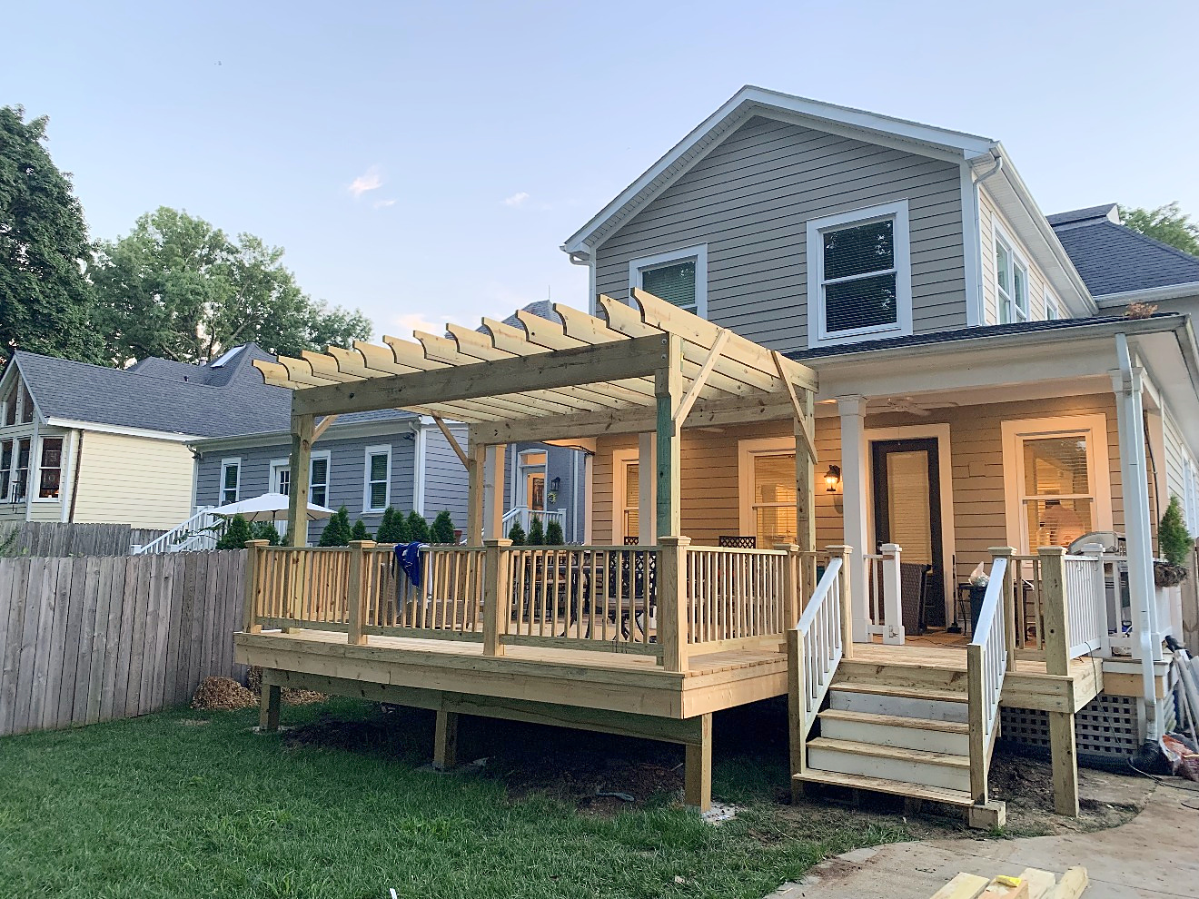 A newly built rear deck with a custom cedar pergola and covered porch at dusk, warm interior lights glowing