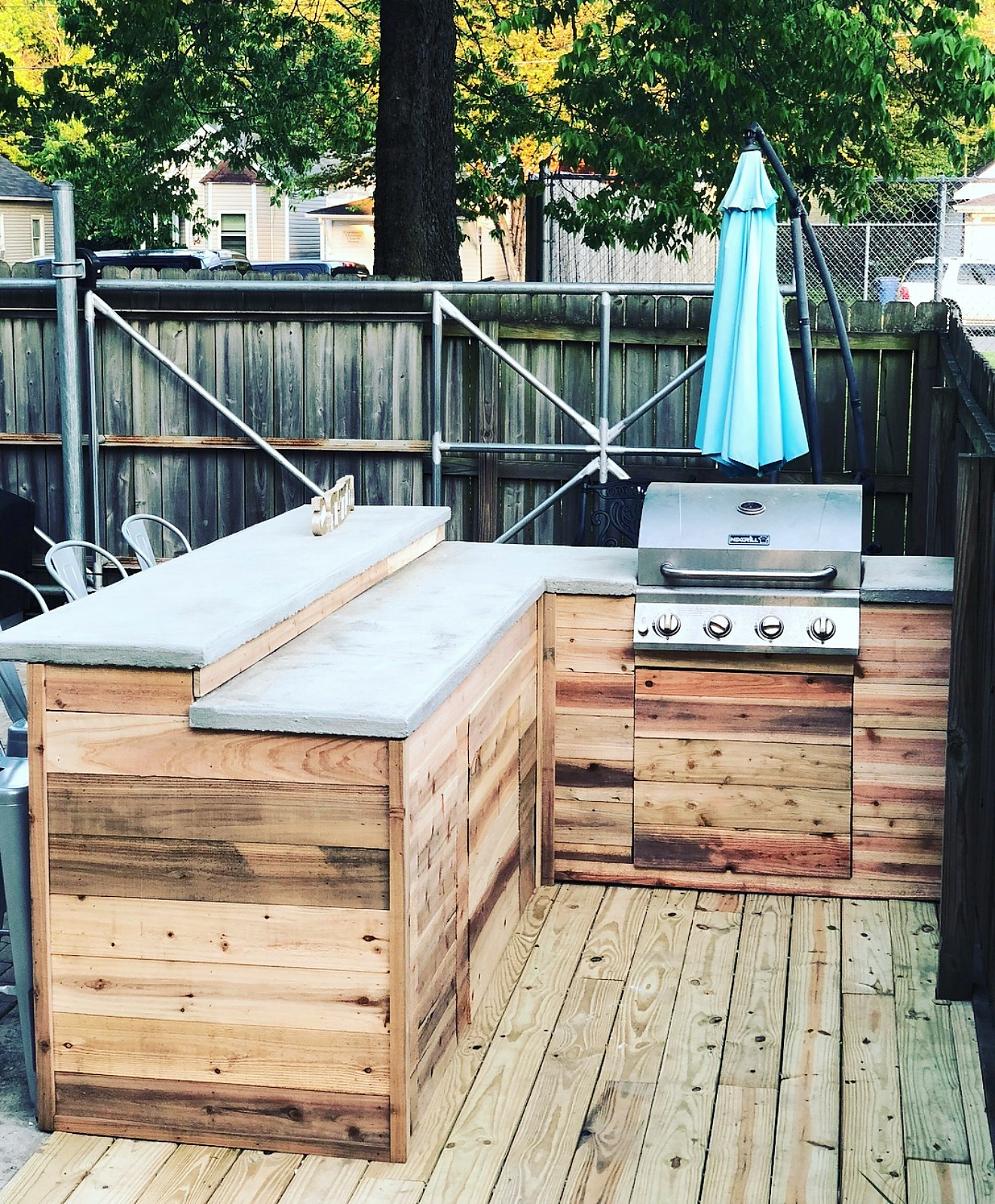 Outdoor kitchen with poured concrete counters, custom wood cladding, and a built-in grill on a pressure-treated deck